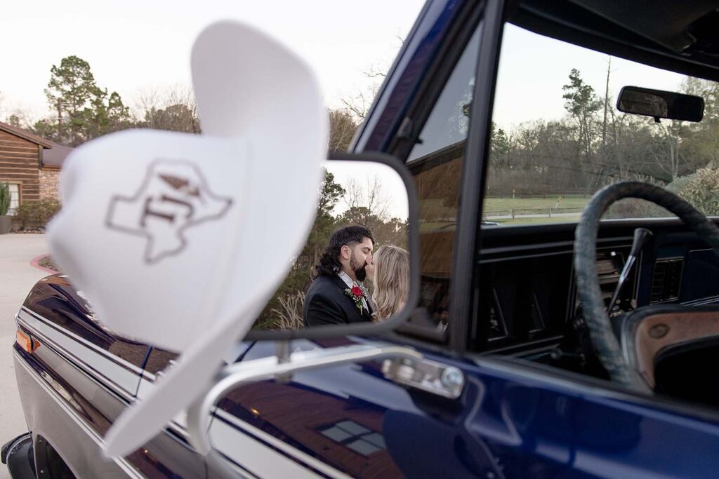 Big Sky Barn wedding: Couple kissing in rearview mirror reflection with branded hat hanging on mirror